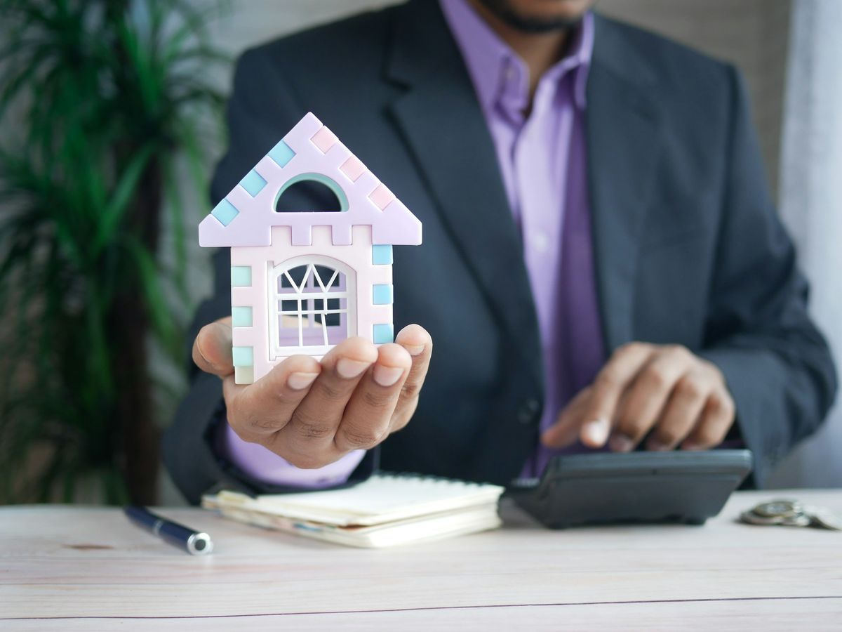 A loan officer holding a small model house next to a calculator